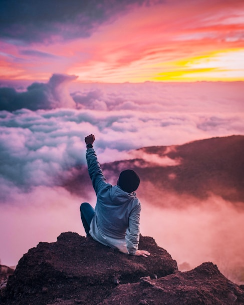 Man sitting on top of a mountain and watching the sunset